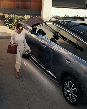 Woman holding purse walking towards driver door of a Moonbow Blue INFINITI QX60 Crossover SUV