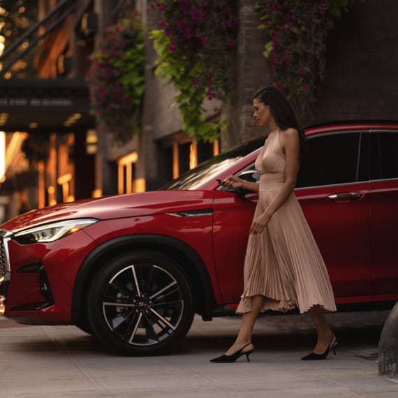 Woman standing beside a red INFINITI SUV, using remote system technology