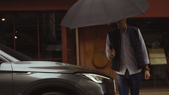 Person Holding Black Umbrella Walking Towards A Metallic Grey Infiniti SUV