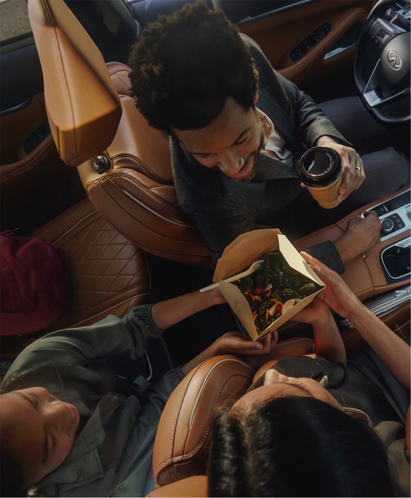 Interior of an INFINITI QX60 highlighting a group of friends sharing food between 2nd row seating and front passenger seat