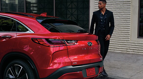 Man walking behind a red INFINITI QX55 Crossover Coupe SUV parked on street