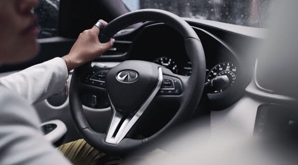 Interior image of INFINITI driver with hand on INFINITI steering wheel
