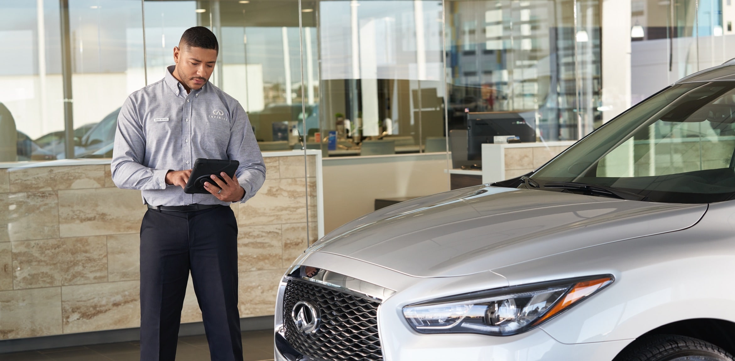 image of a salesperson at an INFINITI retailer working on tablet beside an INFINITI QX60