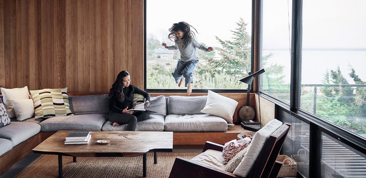 Image of woman sitting on a couch while young girl jumps off couch