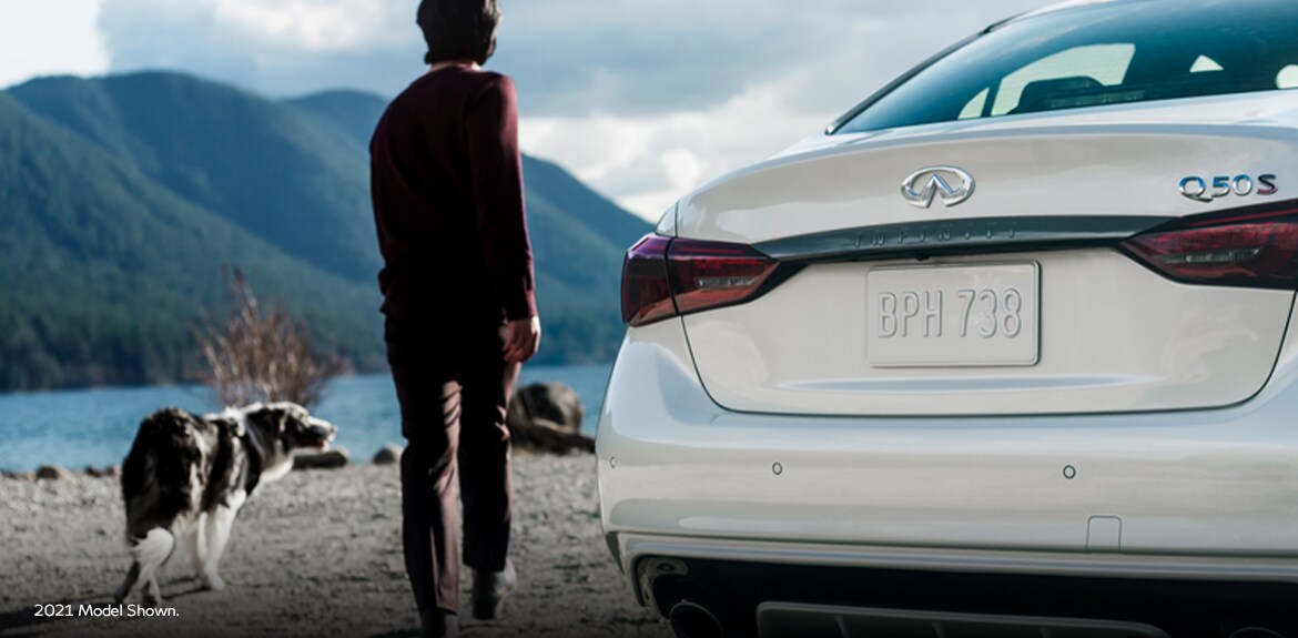 Rear profile view of a man and his dog standing beside the 2022 INFINITI Q50