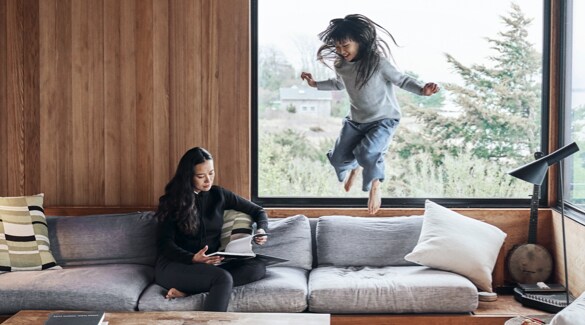 Woman sitting and reading on a white couch while girl jumps off couch