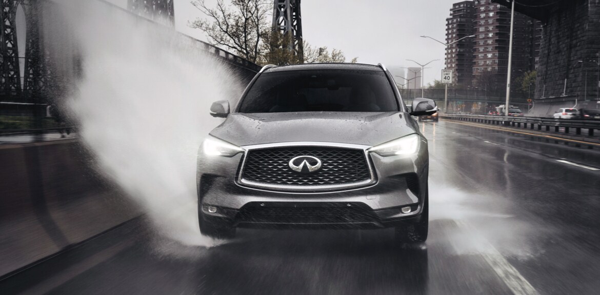 Front profile view of 2023 INFINITI QX50 driving through a puddle highlighting Intelligent AWD feature