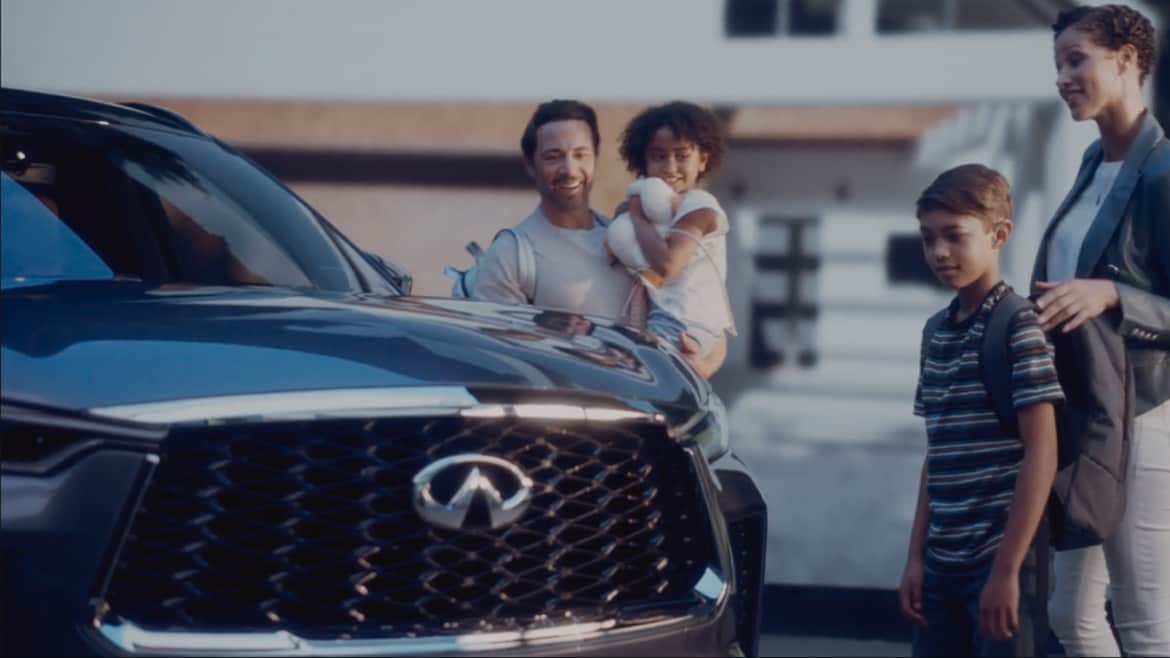 Family standing beside the 2024 INFINITI QX60 shown in Moonbow Blue color