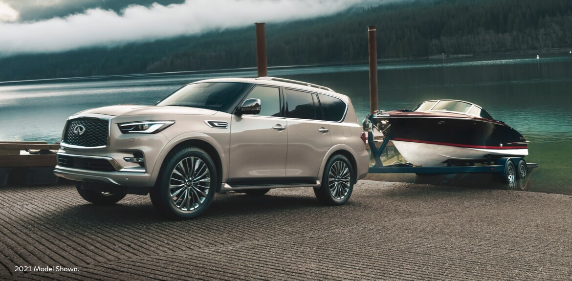 Side profile of 2023 INFINITI QX80 towing a boat highlighting 8500 lb. towing capacity